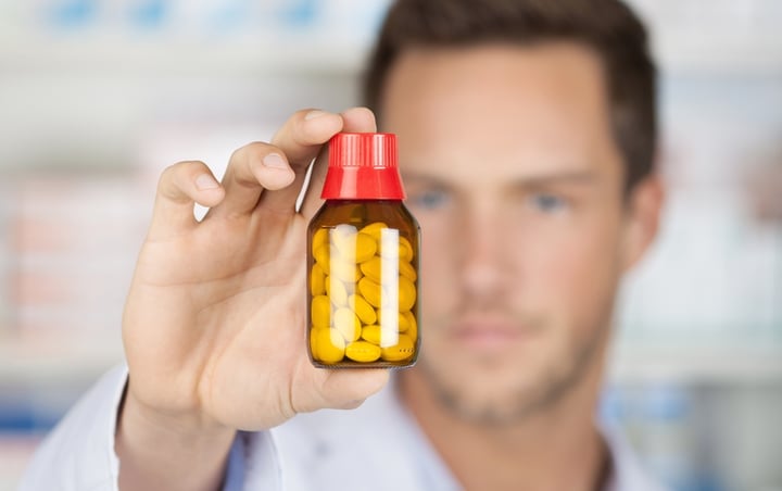 Closeup of a blurred male pharmacist holding out tablets in bottle at drugstore_cut big
